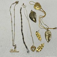Overview of various gold and silver jewelry pieces on white cloth including necklaces, bracelet, and leaf pendants