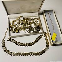 Shot showing all jewelry items including tangled goldtone chains with tiger eye and pearl accents, two goldtone arrowhead-linked necklaces, and boxed delicate gold filled necklace.