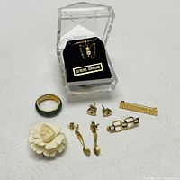 Jewelry items displayed together including the carved flower, green jade ring, various gold-tone earrings, a butterfly pendant in a jewelry box