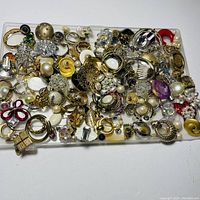 Top view of a large assortment of single costume jewelry earrings and earring parts in mixed colors, styles, and materials on a white surface.