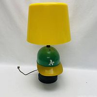 Front view of the Oakland A's baseball cap lamp with yellow lamp shade and power cord.