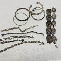 Image showing a group of 8 assorted silver tone bracelets with various designs including twisted bangles, link chains, and embossed wide band bracelet.