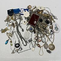 Photo showing an assortment of silvertone costume jewelry necklaces, featuring different chains and pendants on a white surface.