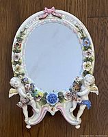 Front view of the oval porcelain mirror showing cherubs and floral decorations on the frame