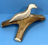 Front-side angle of the carved bird sculpture on Y-shaped antler base against a blue background.