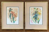 Pair of two abstract floral monoprints framed in gold-tone frames with neutral mats placed side by side on wood surface.