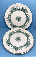 Two green floral patterned plates with embossed scalloped rims shown stacked and individually against blue background.
