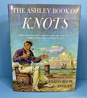 Front cover of 'The Ashley Book of Knots' showing a colorful illustration of a man tying knots on a ship deck with sailing ships and sky background.