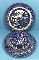 Full set of six Blue Willow china pieces stacked and displayed upright showing the intricate blue and white willow pattern on all items.