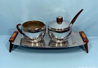 Front angle photo of the entire vintage cream and sugar set with tray, showing shiny silver-tone metal and wooden handles.
