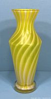 Front full view of the vintage Murano yellow swirl glass vase against a blue background.