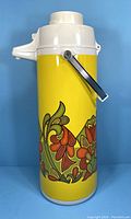 Front side of vintage yellow vacuum thermos with floral design and pump handle