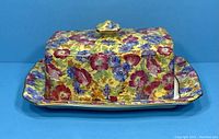 Front view of the lidded butter dish showing colorful floral pattern with gold trim on yellow background.