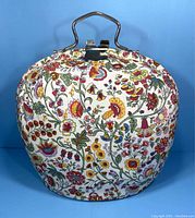 Front view of vintage teapot cozy carrier showing colorful floral fabric and metal handle
