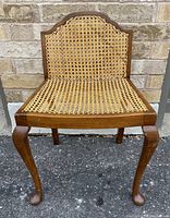 Front view showing wooden frame with woven cane seat and carved legs ending in ball feet.