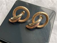 Pair of vintage 10k gold earrings shown side-by-side on a black background, displaying textured circle hoops and tri-tone twisted design.