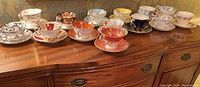 Wide shot of 14 assorted tea cups and saucers arranged on wood sideboard