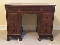 Front view of antique solid walnut desk showing two banks of drawers, carved detailing, round bun feet, and surface wear consistent with age.