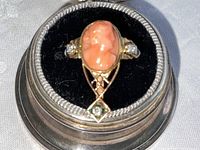 Ring face showing oval carved coral cameo in yellow gold setting with black velvet beneath