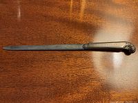 Full view of the letter opener placed on a wood surface, showing the shape and detailing of the handle and blade.