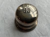 Closed top view of round box showing domed lid with raised “BB” logo and surface tarnish