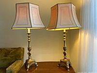 Front view of both lamps side by side on wooden table against wall.