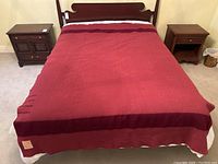 Full view of the blanket spread on a bed showing wild cranberry color with darker horizontal stripes and original label sewn on corner.