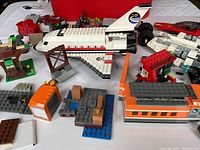 View of assorted assembled LEGO items including large white space shuttle, orange boxcar, small constructions and minifigures