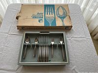 Flatware set arranged in original plastic tray with cardboard box included, showing organized compartments for each type of utensil.