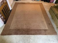 Top-down view of entire rug on light carpet showing darker border, lighter center, and wear spots