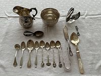 Overview of all items in lot: creamer, sugar bowl, swan salt cellar, sugar tongs, serving utensils and spoons