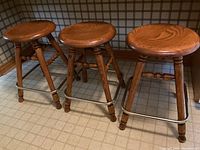 Front view of three oak swivel bar stools side by side showing seats and bases.