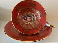 View of fruit cup placed in the saucer showing dark orange color with gold detailing and central painted fruit medallion.