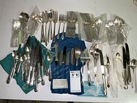 Wide view of the entire flatware collection laid out on table, showing variety of forks, knives, spoons, some wrapped in tissue.