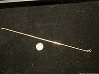 Full view of gold bracelet laid flat against black background with a coin beside it for scale.