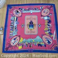 Full view of large square silk scarf laid flat, showing coral pink center and blue border with detailed Paris illustrations.