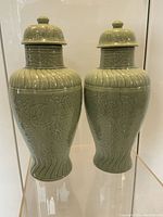 Front view of two vintage celadon ceramic vases with lids showing their shape and embossed design.
