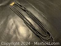 Photo of triple strand hematite bead necklace laid on black leather surface showing full length including clasp.