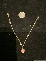 Photo of the vintage 14K yellow gold bracelet with small pearls and heart-shaped charm on black background, with a quarter for size reference.