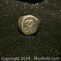 Front view of vintage sterling silver ring with engraved initial 'R' on face, displayed on black fabric to highlight details and condition.