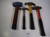 Top view of four hammers varied in size and handle color: blue mallet, yellow handle claw hammer, red handle claw hammer, small black handle claw hammer.