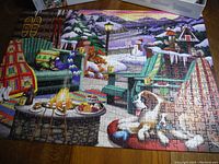 Completed Ravensburger 500-piece jigsaw puzzle showing a colorful winter scene with a dog by a fire pit and Adirondack chairs outdoors