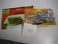 Two unopened packs of drop-shot soft plastic baits: one Berkley PowerBait 3-inch Twitchtail Minnow 12 count, black shad color; one TriggerX 4-inch Minnow 8 count, sandre/zander color