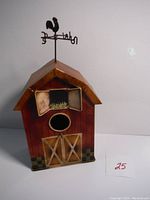 Front view of the tin birdhouse barn with doors, round entrance, window with flower box, and rooster weather vane on top.