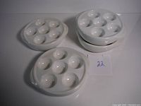 Four white ceramic escargot dishes photographed together showing six indentations per dish and stackable design.