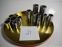 Photo showing an assortment of 16 grey metal sockets on a circular brass plate with note '21'
