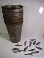 Seven stacked metal sap buckets with rust and wear, along with fifteen metal sap taps spread out around the buckets.