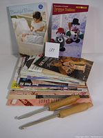 Wide shot of crochet and knit pattern books stacked alongside two large wooden crochet hooks with metal tips.