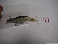Black and silver Rapala Shad Rap fishing lure with clear plastic lip and treble hooks shown on white background with lot number 79.