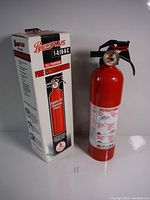 Red Pyrene Plus fire extinguisher next to its white product box showing extinguisher design and labeling.